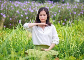 Woman meditating in a field of flowers focusing on well-being.