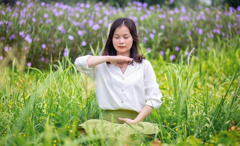 Woman meditating in a field of flowers focusing on well-being.