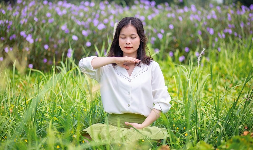 Woman meditating in a field of flowers focusing on well-being.