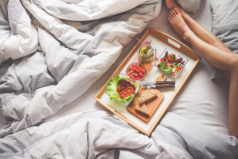 Breakfast tray with salad and juice on bed, relaxing morning.