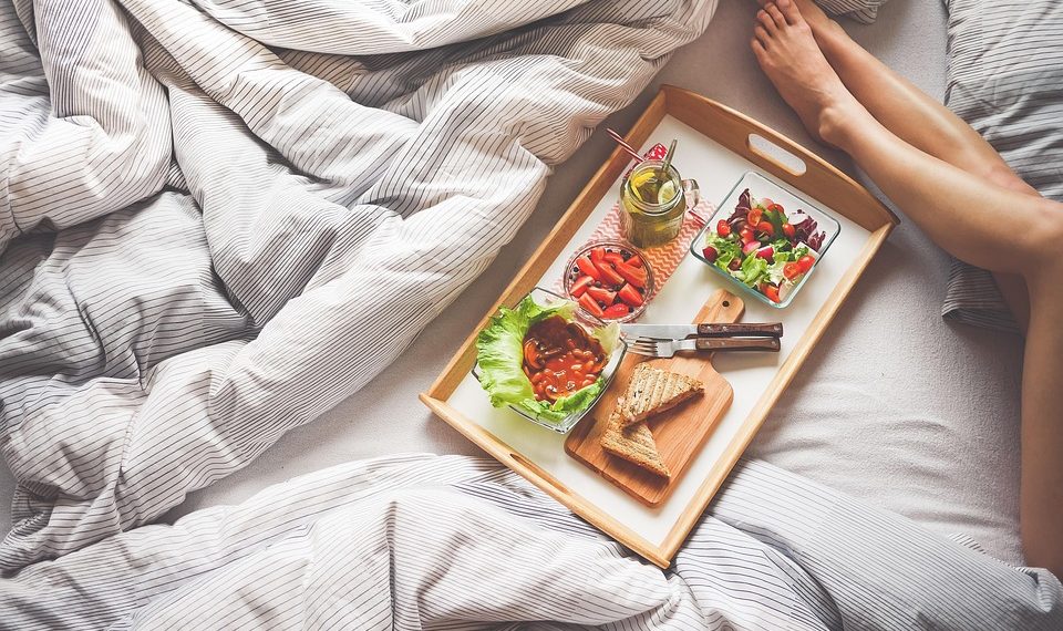 Breakfast tray with salad and juice on bed, relaxing morning.