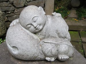 Sleeping monk stone statue in a peaceful garden setting.