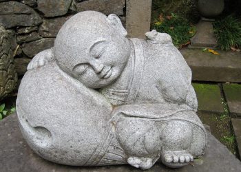 Sleeping monk stone statue in a peaceful garden setting.