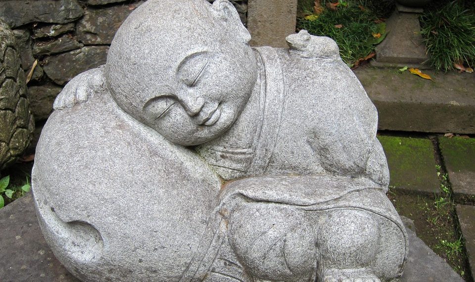 Sleeping monk stone statue in a peaceful garden setting.