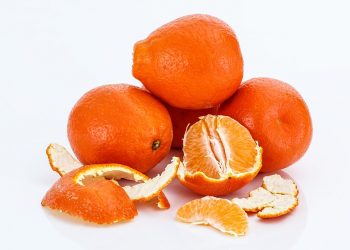 Mandarins stacked, one peeled revealing juicy segments.