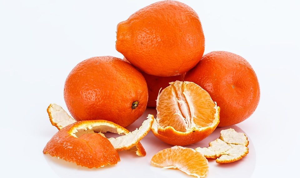 Mandarins stacked, one peeled revealing juicy segments.