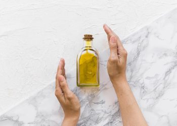 Hands holding a bottle of olive oil on a marble surface.