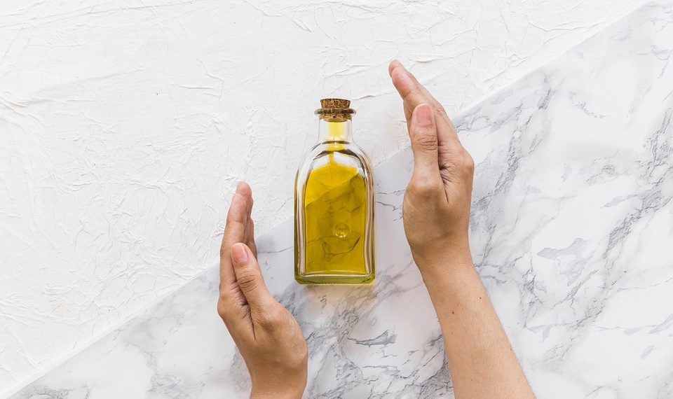 Hands holding a bottle of olive oil on a marble surface.