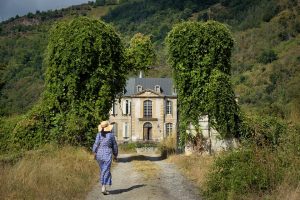 Woman in a blue dress walks toward a historic mansion.