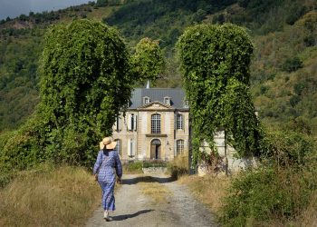 Woman in a blue dress walks toward a historic mansion.