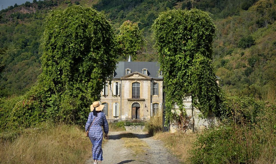 Woman in a blue dress walks toward a historic mansion.