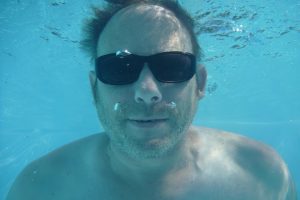 Underwater man wearing sunglasses swimming.