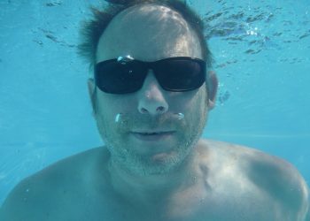 Underwater man wearing sunglasses swimming.