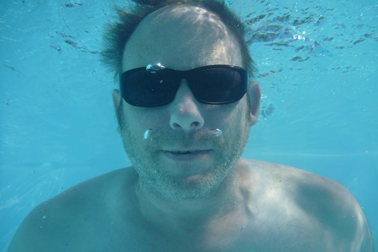 Underwater man wearing sunglasses swimming.