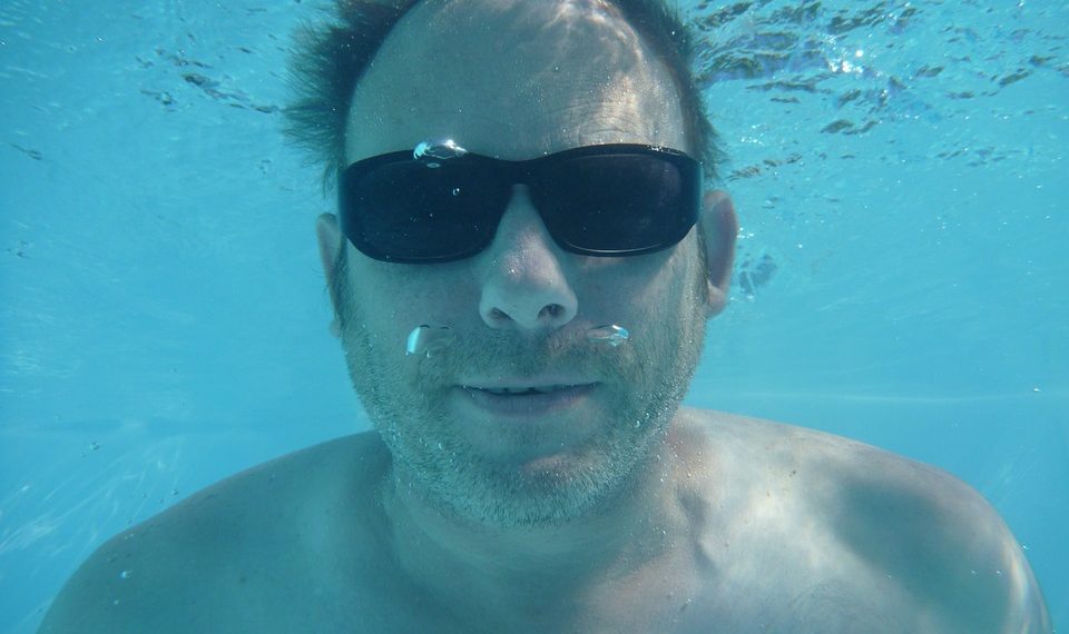 Underwater man wearing sunglasses swimming.