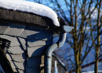 Snow-covered roof with icicles hanging from a curved gutter.