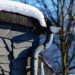Snow-covered roof with icicles hanging from a curved gutter.