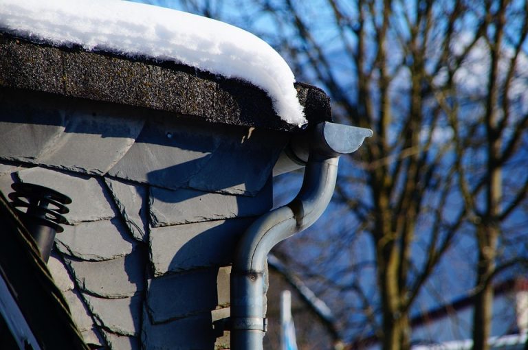 Snow-covered roof with icicles hanging from a curved gutter.