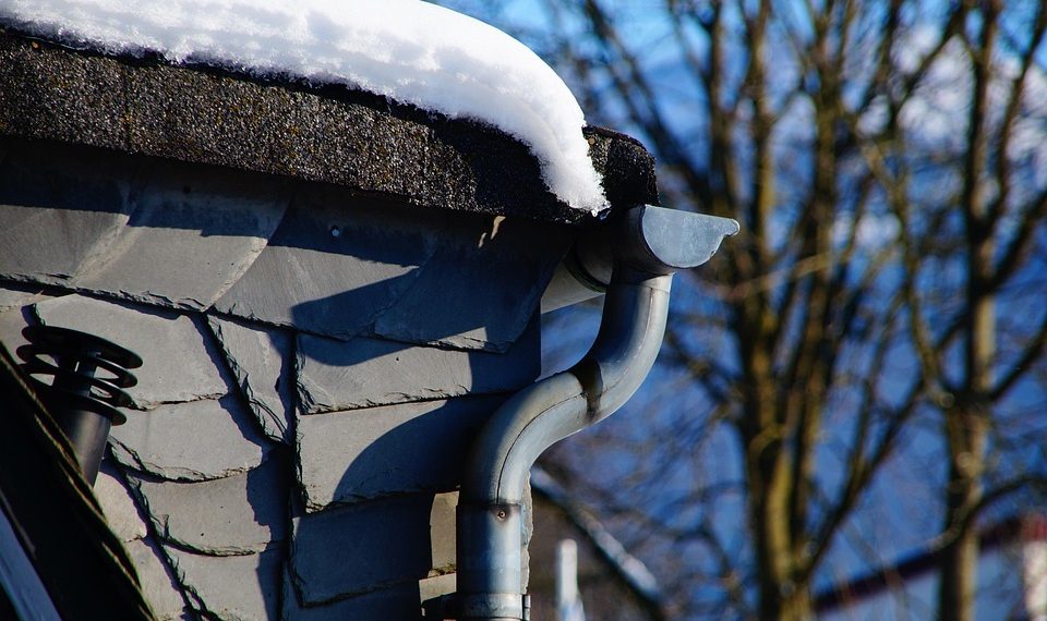 Snow-covered roof with icicles hanging from a curved gutter.