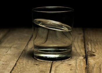 Glass of water half full on wooden table.