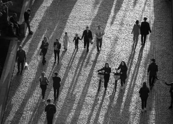 People walking and cycling on a sunlit cobblestone street.
