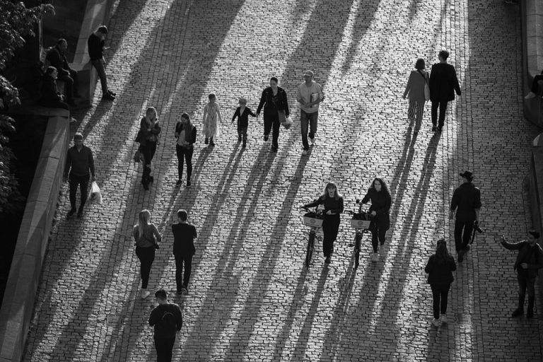 People walking and cycling on a sunlit cobblestone street.