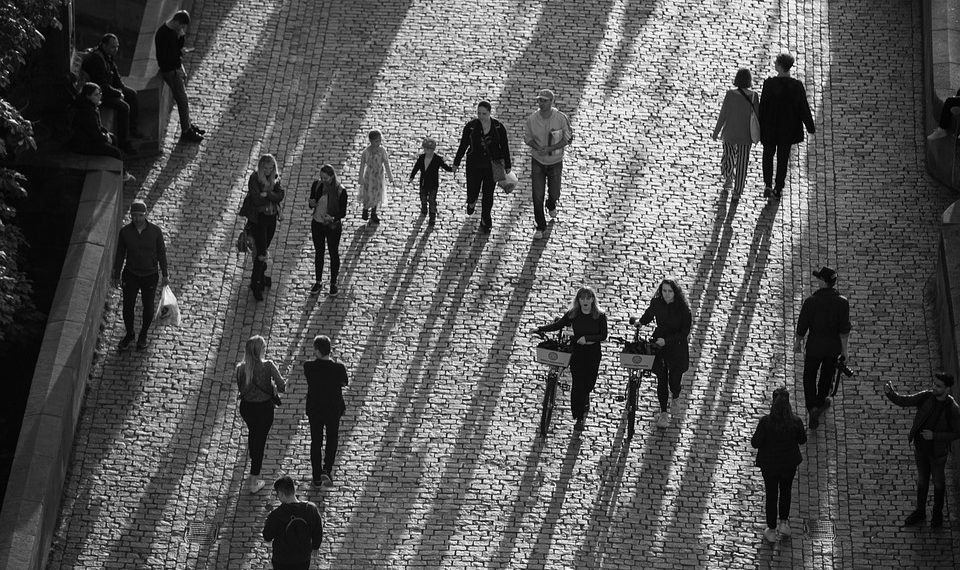 People walking and cycling on a sunlit cobblestone street.