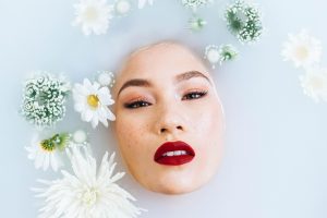 Woman with vibrant red lips immersed in a floral milk bath.