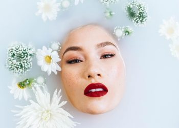 Woman with vibrant red lips immersed in a floral milk bath.