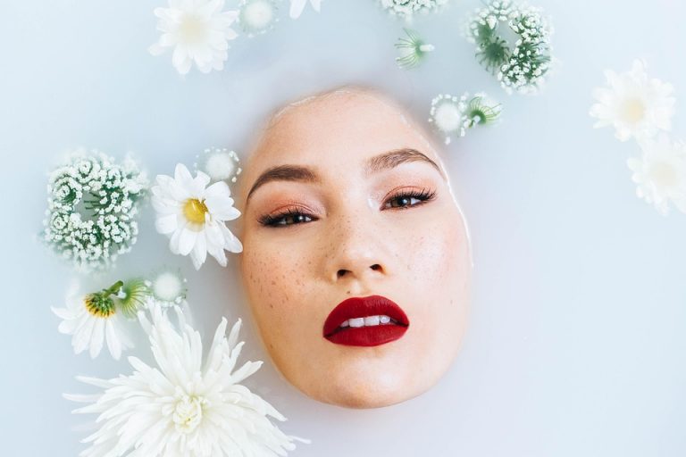 Woman with vibrant red lips immersed in a floral milk bath.