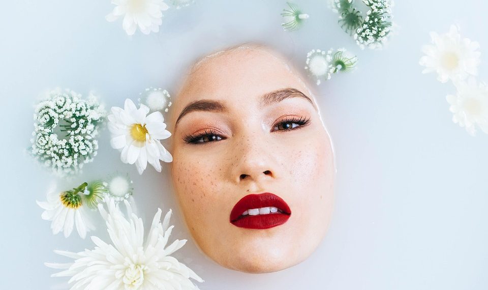 Woman with vibrant red lips immersed in a floral milk bath.