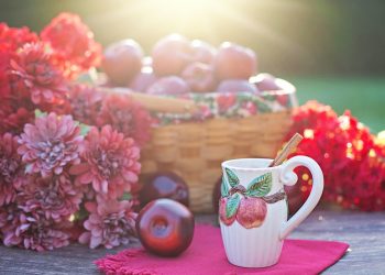 Basket of apples with flowers and cinnamon apple mug on a sunny table.