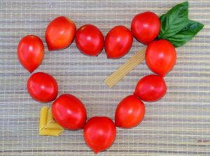 Cherry tomatoes and pasta form a heart shape on a woven mat.