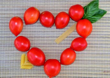 Cherry tomatoes and pasta form a heart shape on a woven mat.