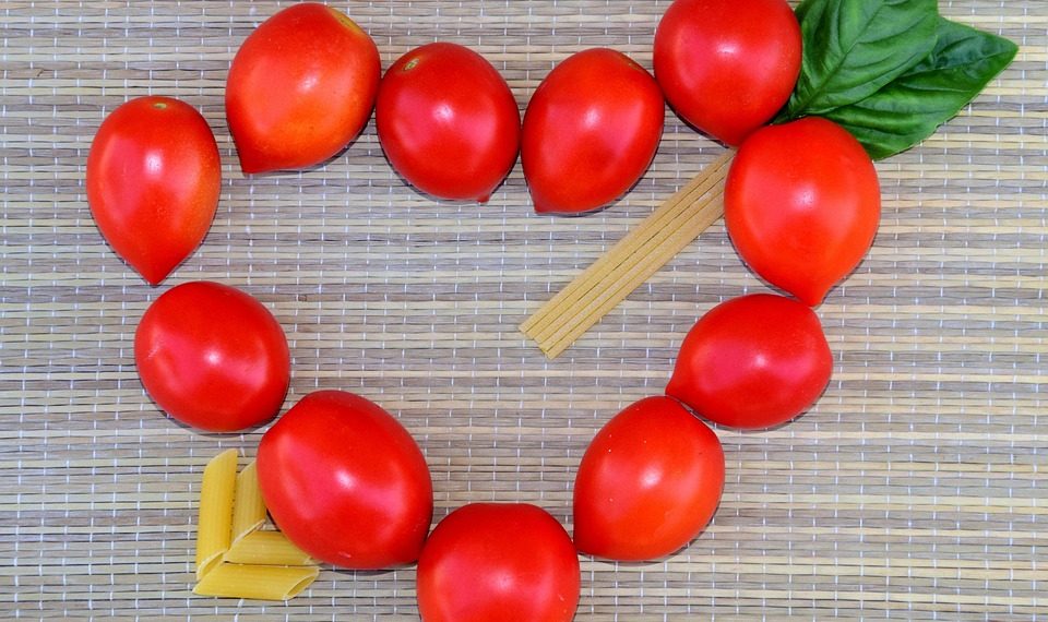 Cherry tomatoes and pasta form a heart shape on a woven mat.