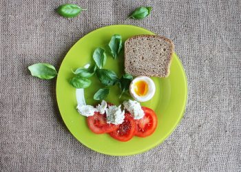 Tomato, basil, soft-boiled egg, and bread on a green plate.