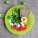 Tomato, basil, soft-boiled egg, and bread on a green plate.