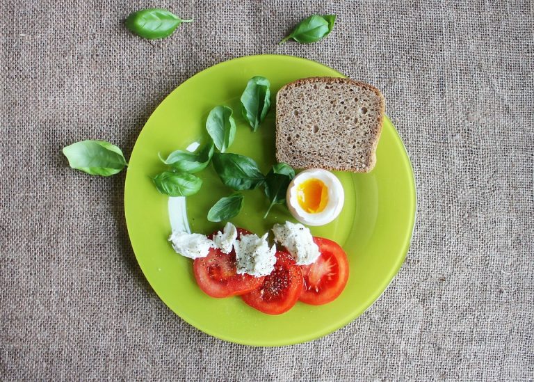 Tomato, basil, soft-boiled egg, and bread on a green plate.