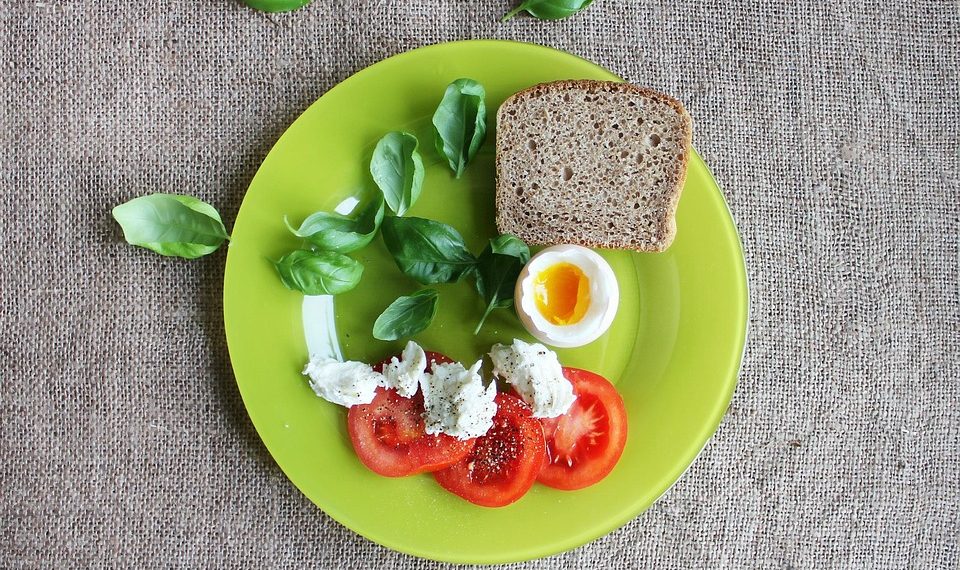 Tomato, basil, soft-boiled egg, and bread on a green plate.