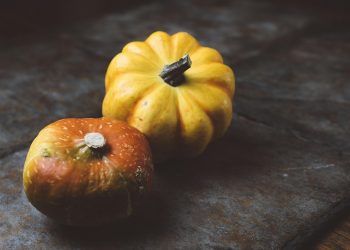 Two small pumpkins on a rustic table surface.