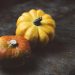 Two small pumpkins on a rustic table surface.