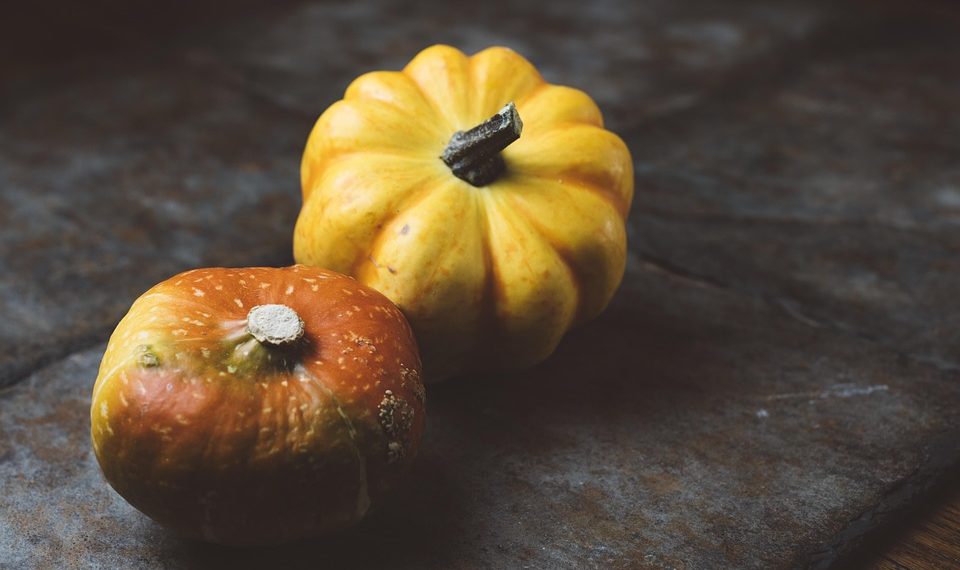 Two small pumpkins on a rustic table surface.
