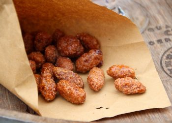 Caramelized almonds in a brown paper bag on a wooden table.