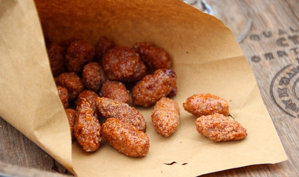Caramelized almonds in a brown paper bag on a wooden table.