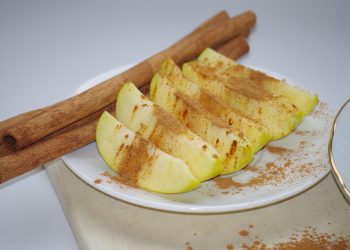 Apple slices with cinnamon and whole cinnamon sticks on a plate.