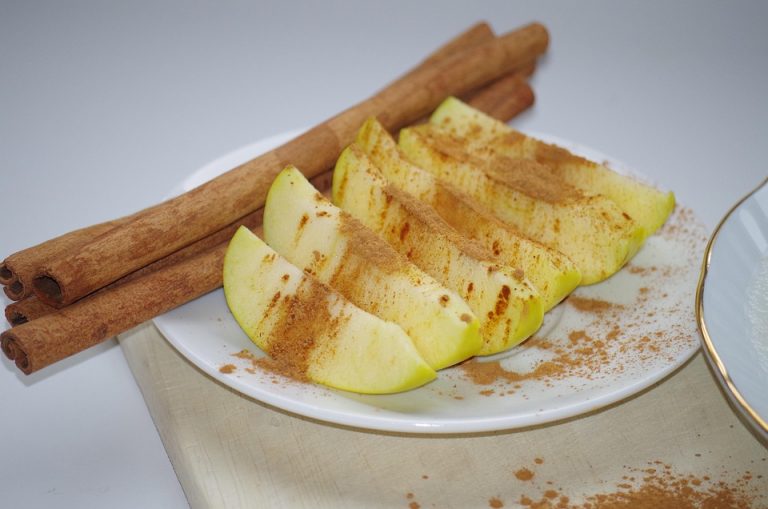 Apple slices with cinnamon and whole cinnamon sticks on a plate.