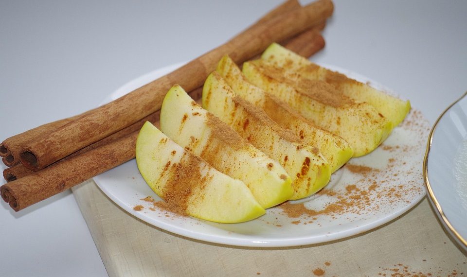 Apple slices with cinnamon and whole cinnamon sticks on a plate.