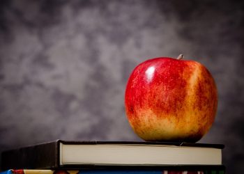Red apple resting on a stack of books.