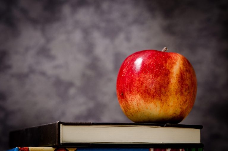 Red apple resting on a stack of books.