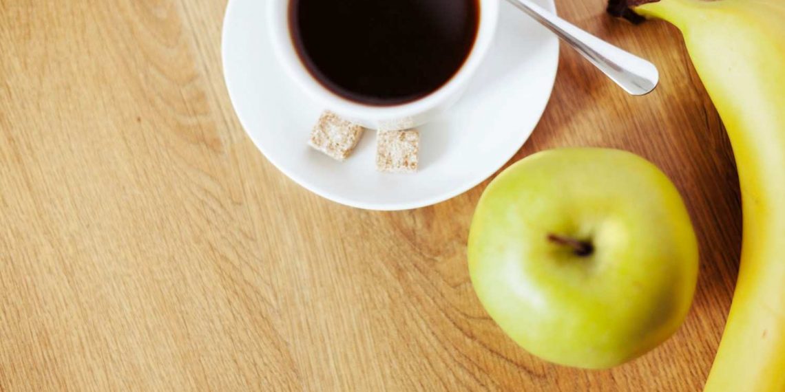 Coffee with sugar cubes, green apple, and banana on wooden table.